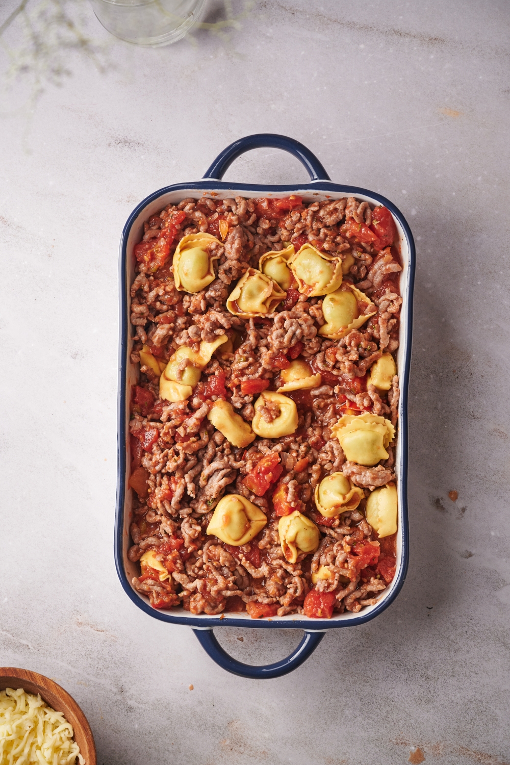 A baking dish filled with cooked ground beef, tomato sauce, and stuffed tortellini.