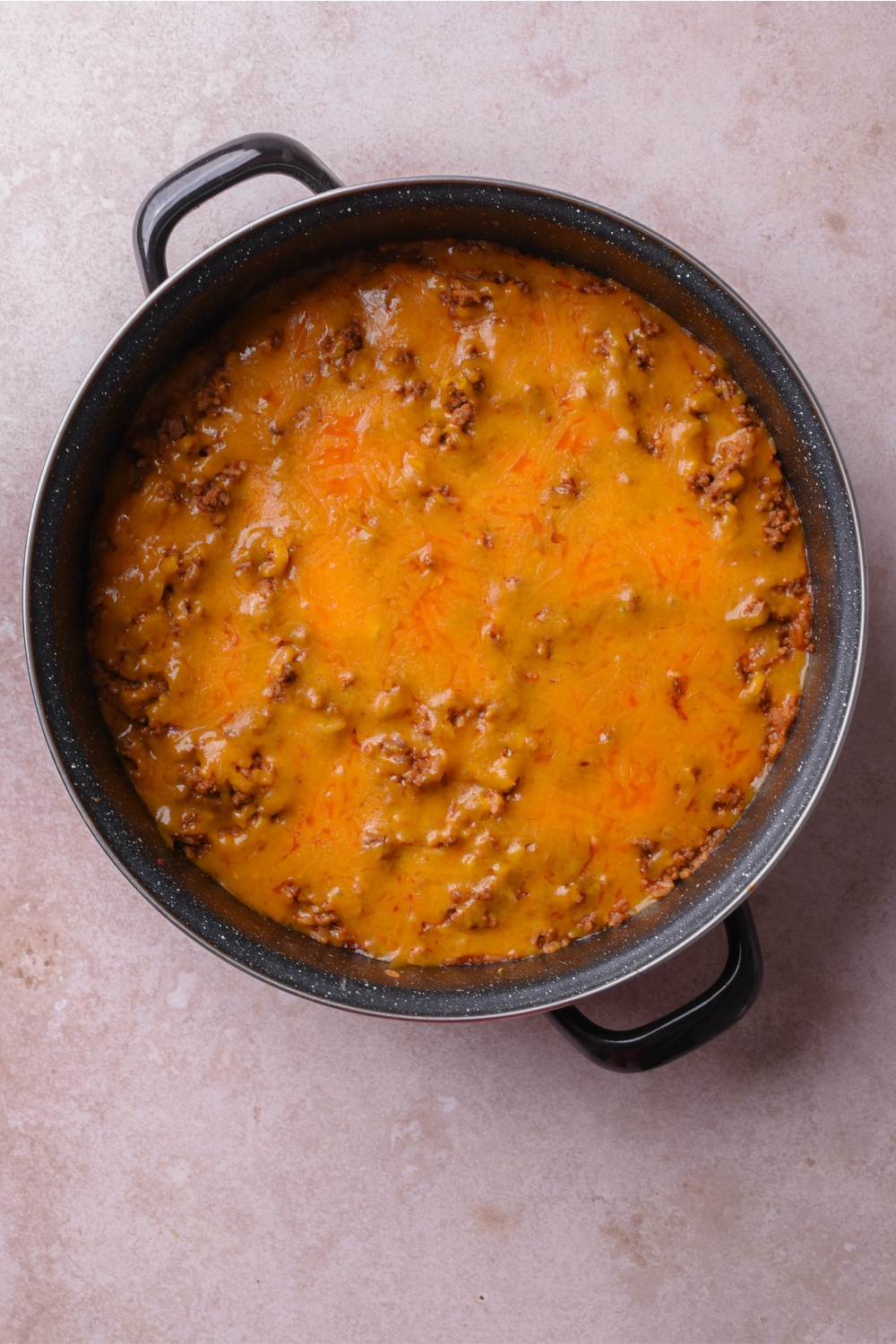 A skillet filled with cooked and seasoned ground beef covered in a layer of melted cheese.