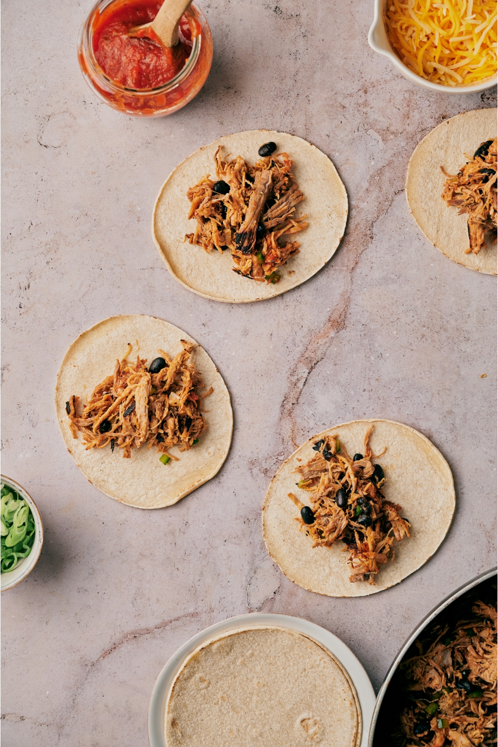 Four tortillas filled with pork, black beans, and veggies. The tortillas are surrounded by an assortment of ingredients.