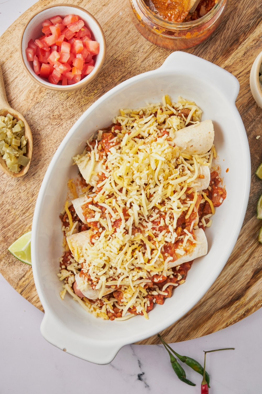 A white baking dish filled with hot dogs wrapped in tortillas on a bed of chili covered in shredded cheese.