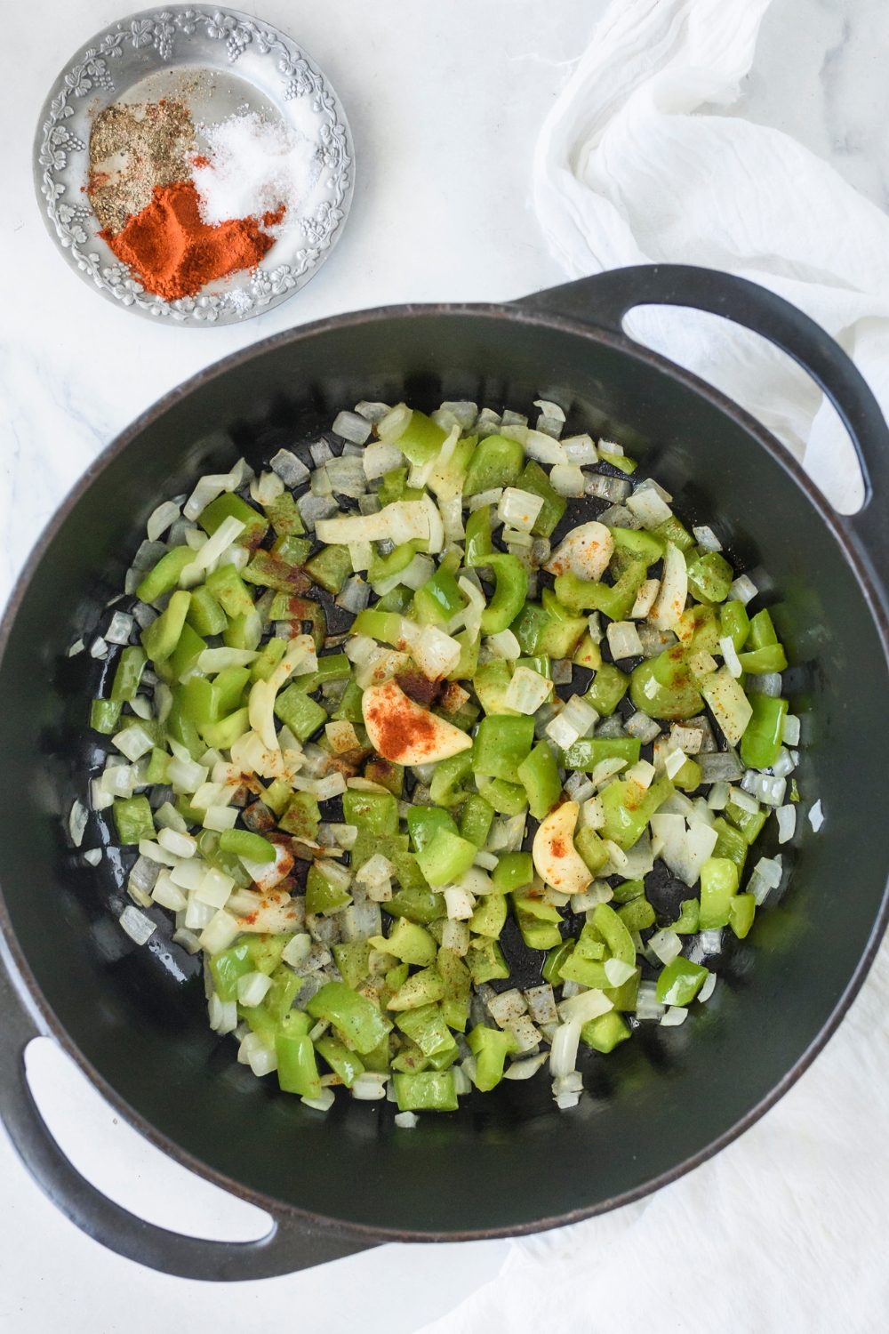 A pot filled with diced green peppers, onion, garlic, and spices added but not yet mixed together.