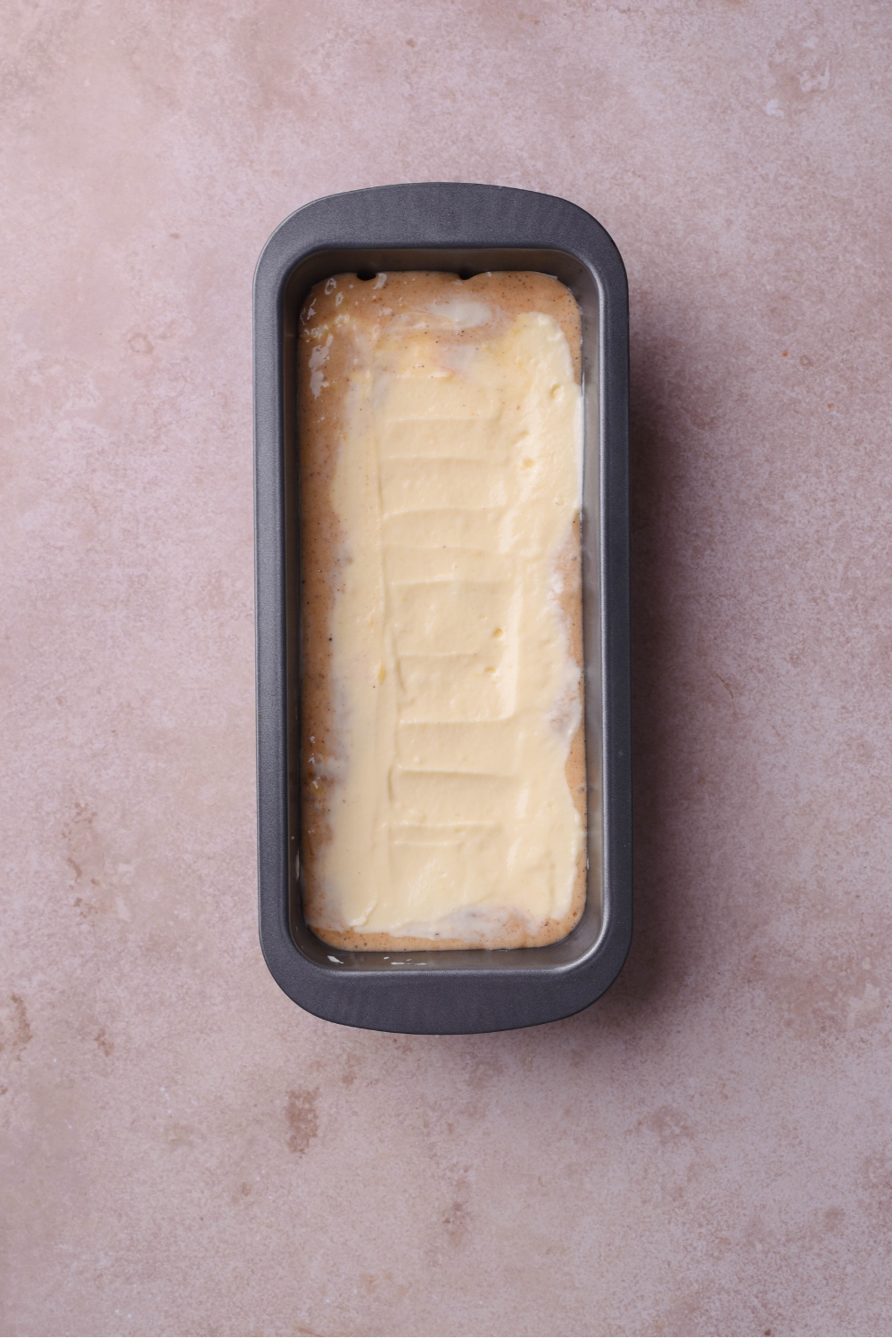 A loaf pan filled with banana bread batter and a layer of cream cheese spread over top.