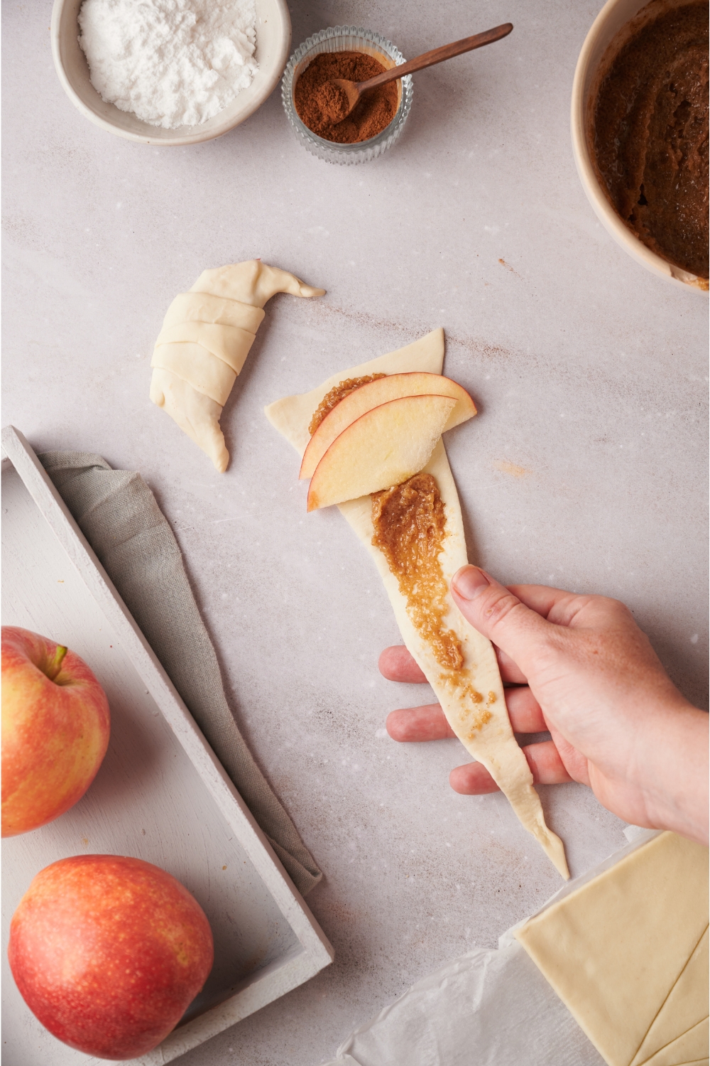 A hand rolling brown sugar and apple wedges in crescent roll dough.