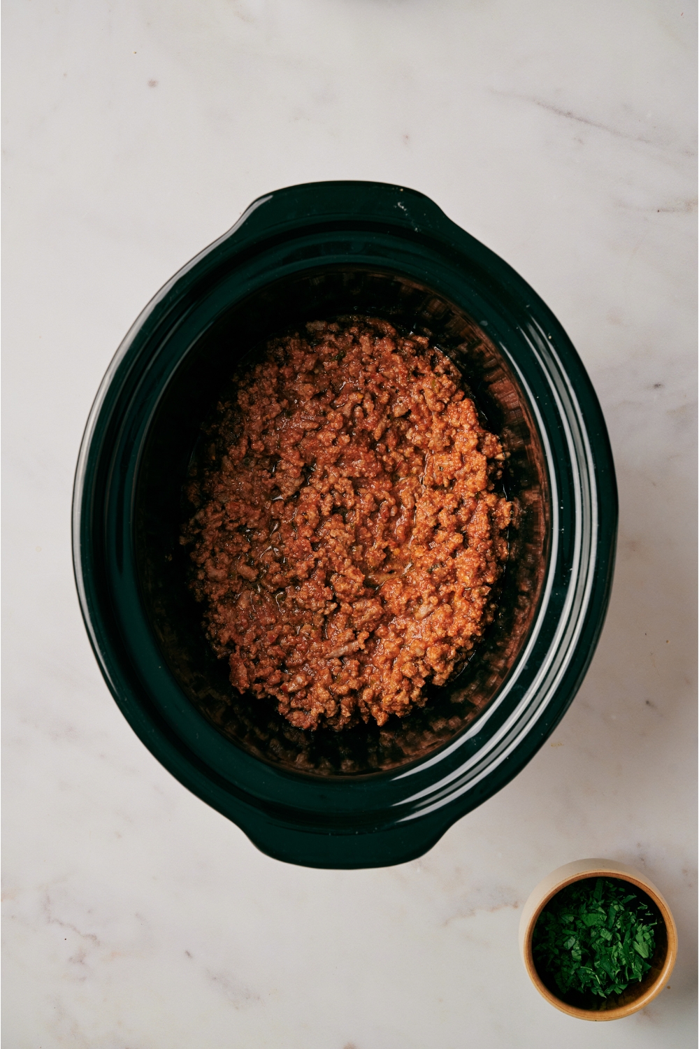 A slow cooker filled with cooked and seasoned ground beef.