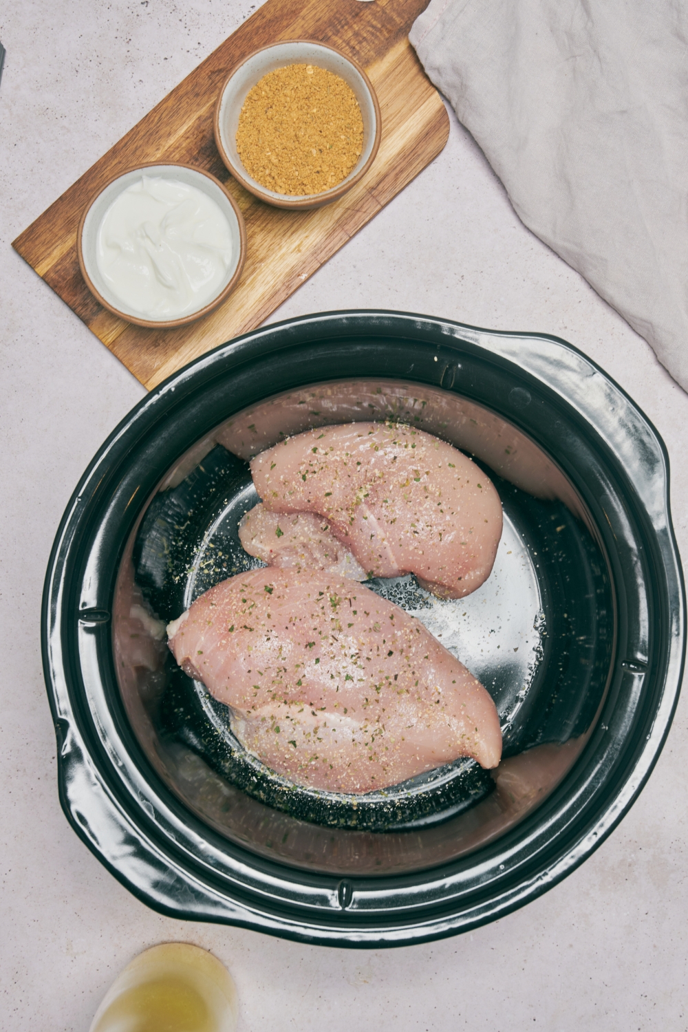 Two raw seasoned chicken breasts in the bottom of a slow cooker.