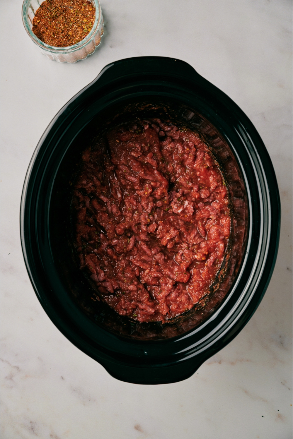 A slow cooker filled with raw ground beef.