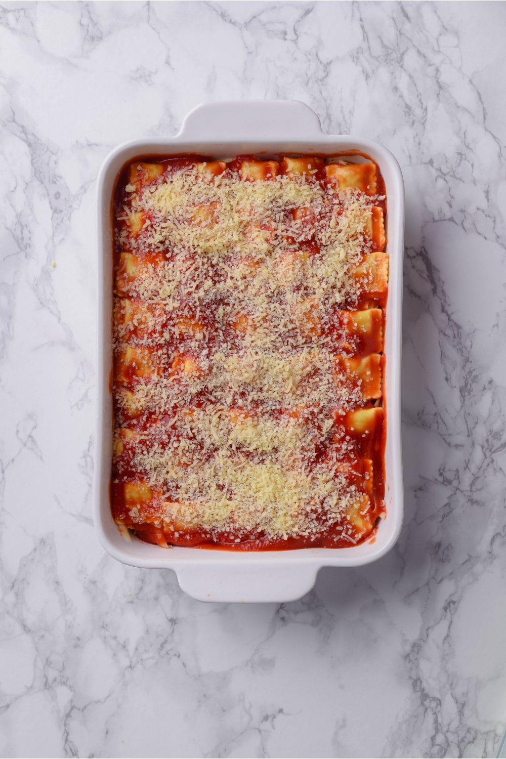 A baking dish filled with ravioli casserole topped with grated parmesan cheese.