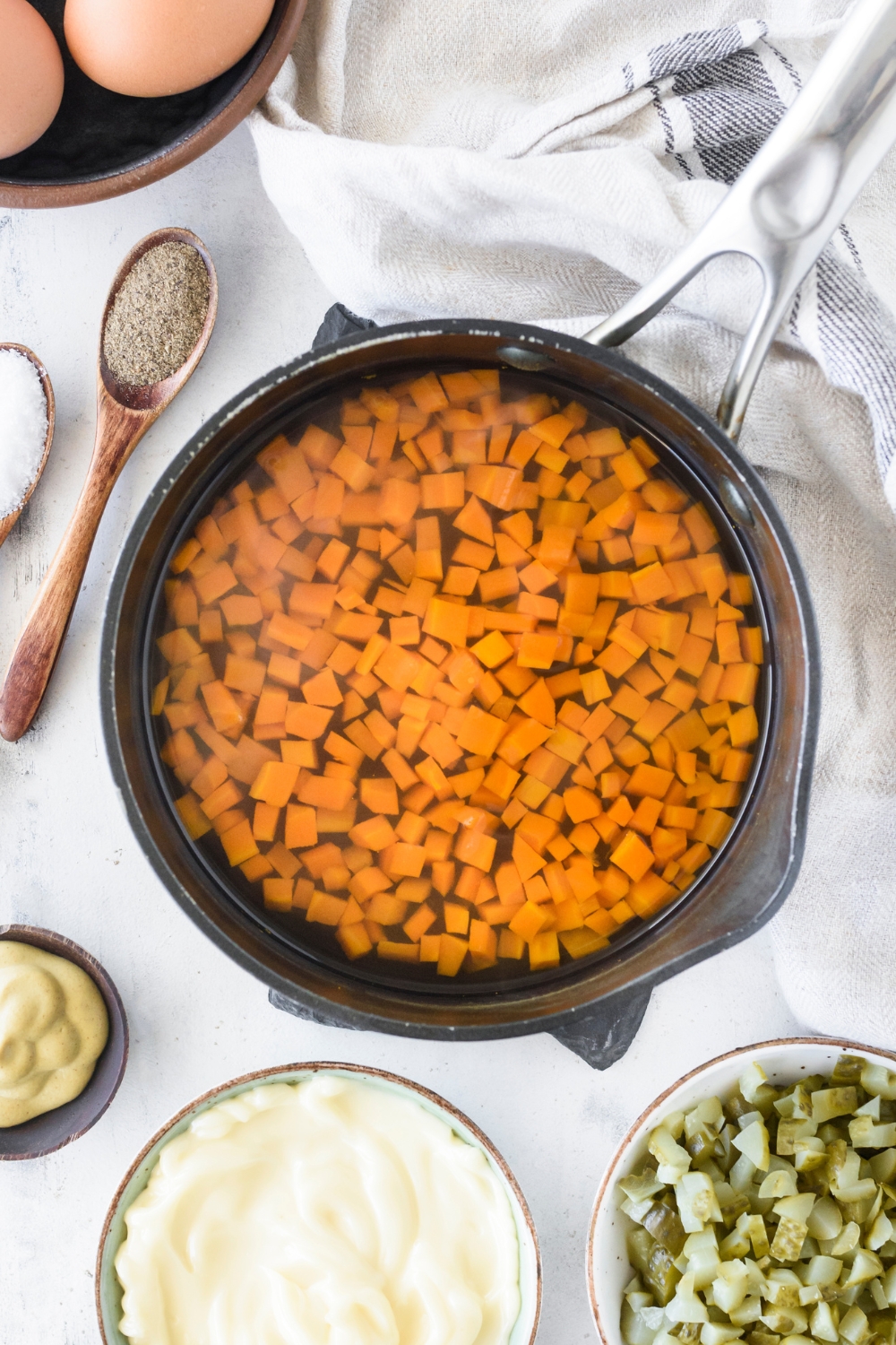 A pot of diced carrots in water surrounded by an assortment of ingredients.