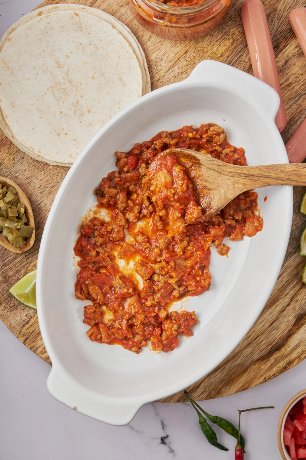 A baking dish with chili added using a wooden spoon.