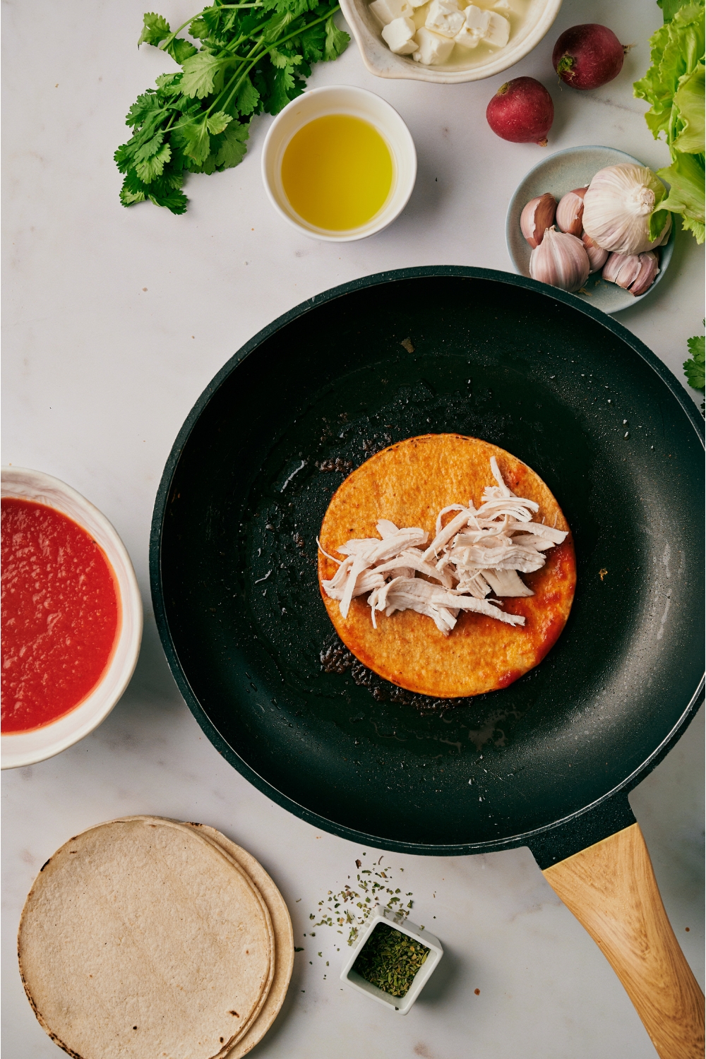 A skillet with a red tortilla and a pile of shredded chicken is on top of the tortilla.