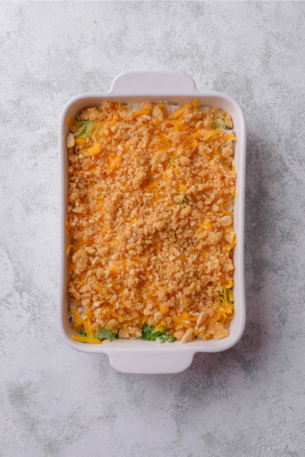 A baking dish filled with unbaked ham casserole covered in a crushed cracker topping.