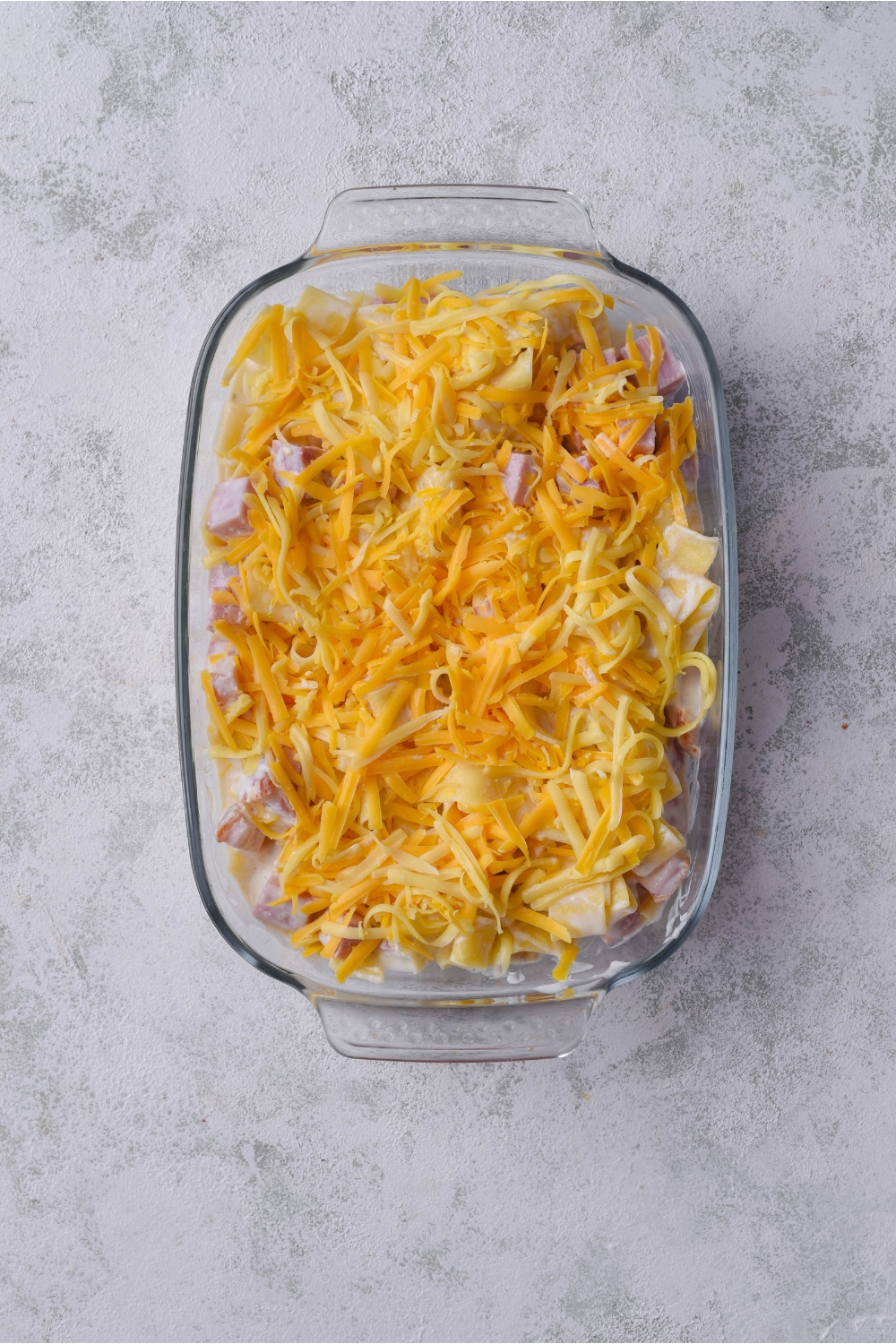 A baking dish filled with ham and noodle casserole covered in a layer of shredded cheese.