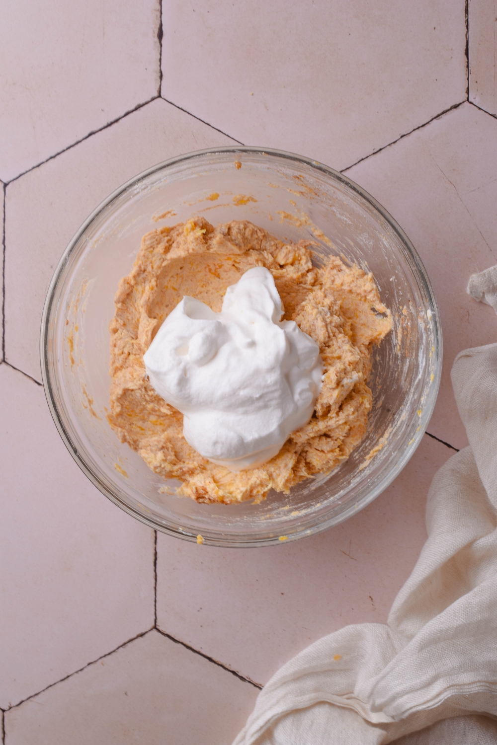 A clear bowl filled with pumpkin cream cheese dip and a scoop of whipped cream has been added but not yet combined.