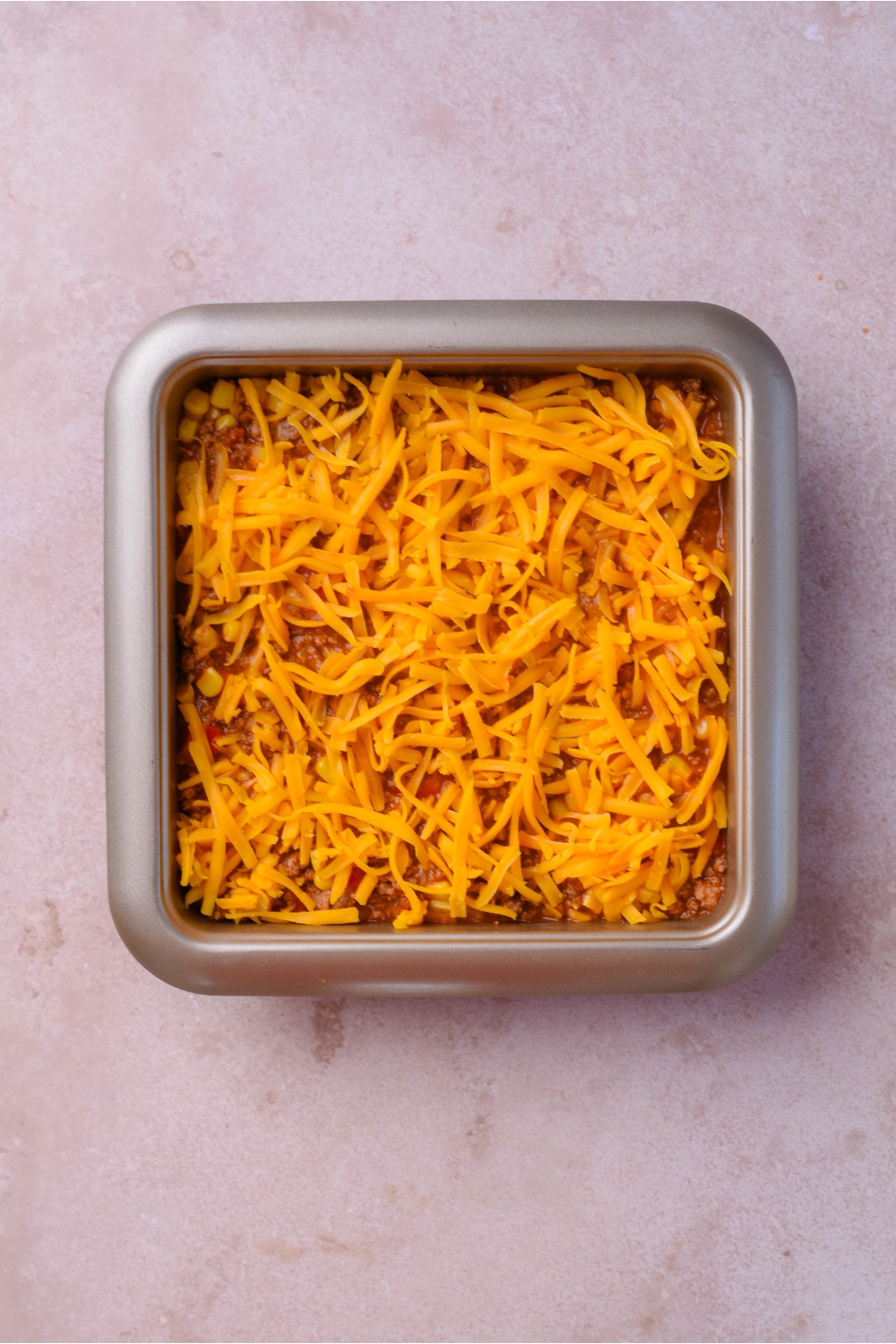 A square baking dish filled with sloppy joe casserole covered in shredded cheese.
