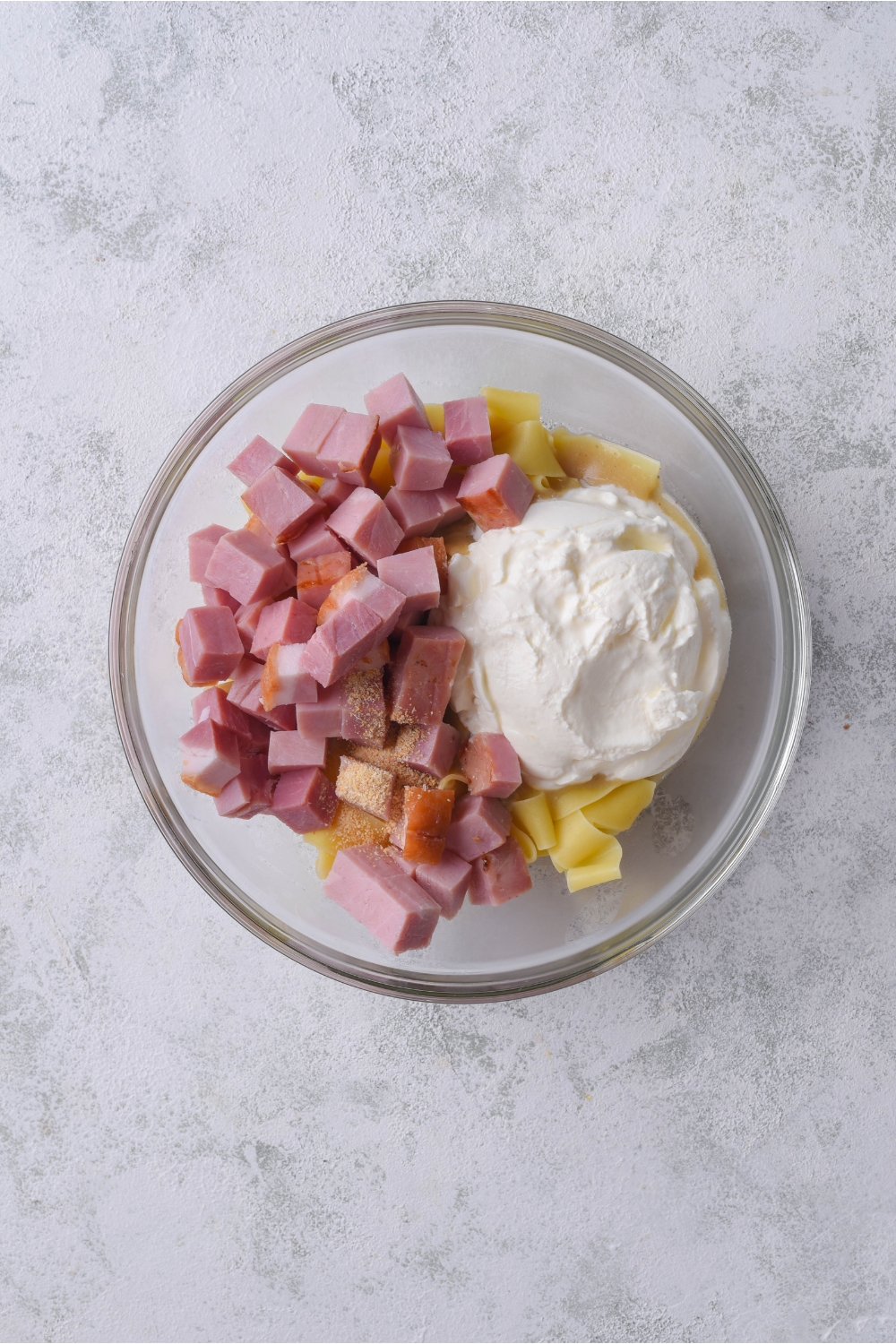 A bowl of egg noodles topped with diced ham, garlic powder, and sour cream.