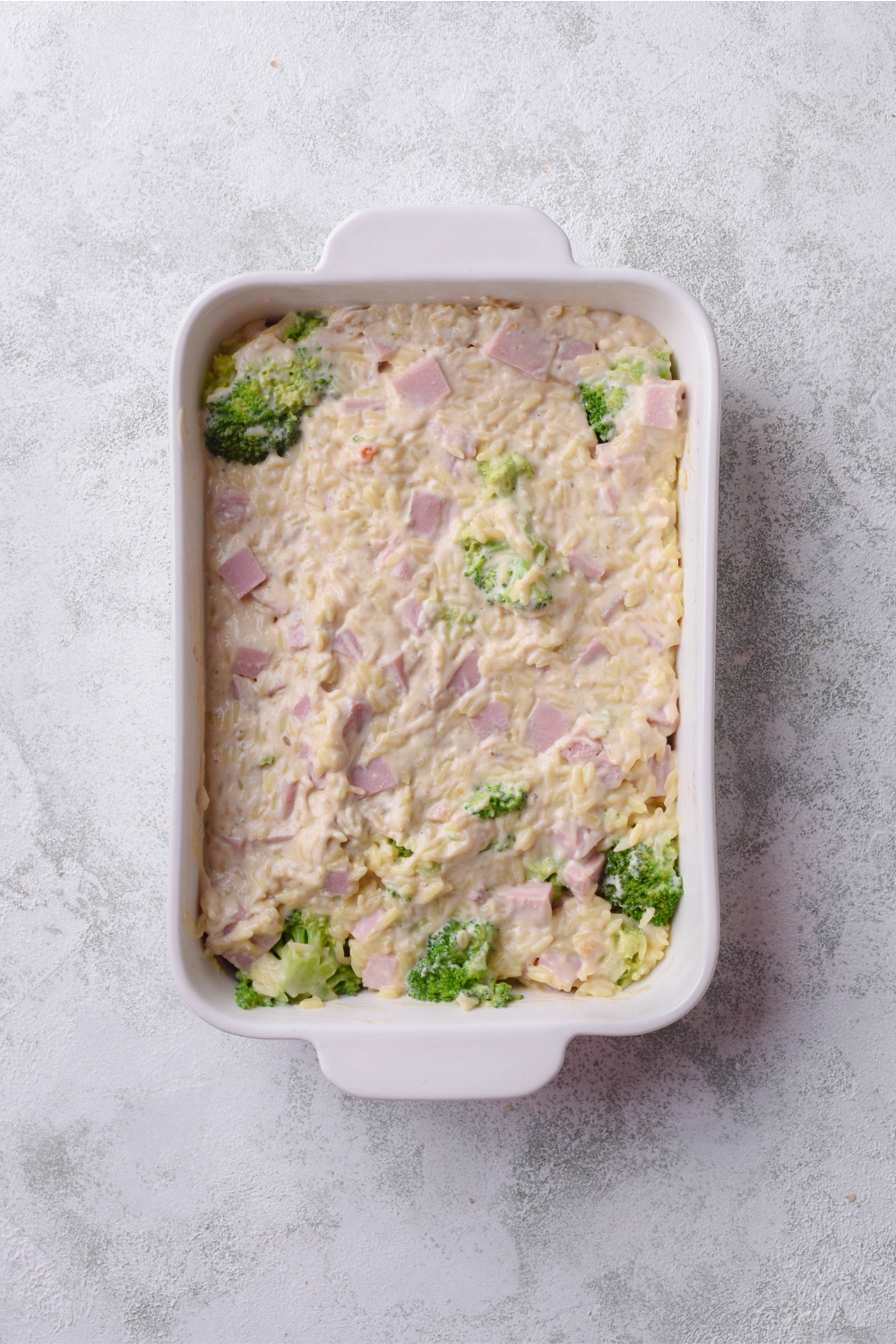 A baking dish filled with unbaked ham, broccoli, and rice casserole.