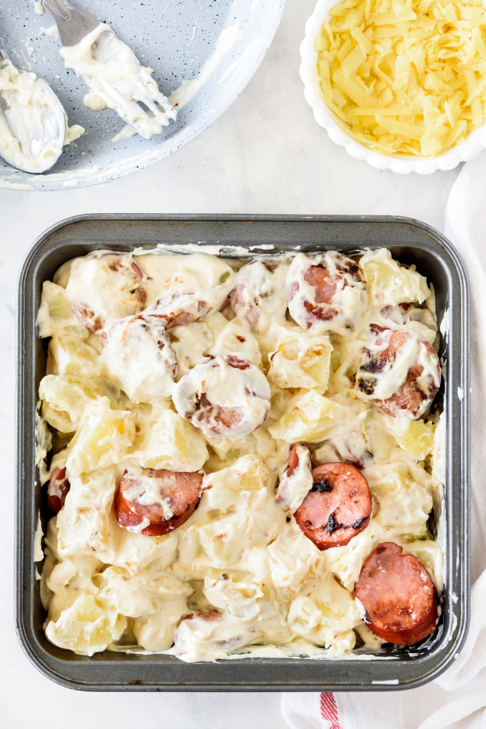 A baking dish filled with sausages and potatoes covered in a cream sauce.