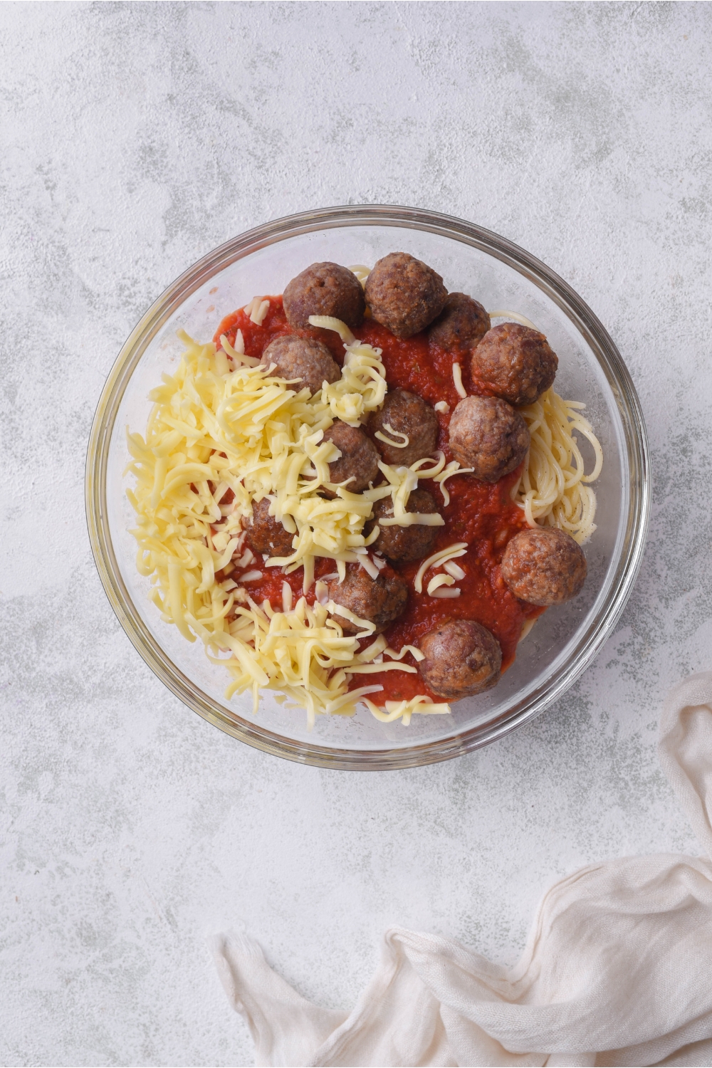 A bowl filled with spaghetti noodles, red sauce, meatballs, and shredded cheese.