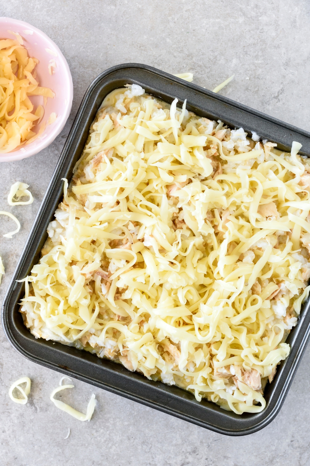 A baking dish filled with canned tuna and white rice covered in shredded cheese.