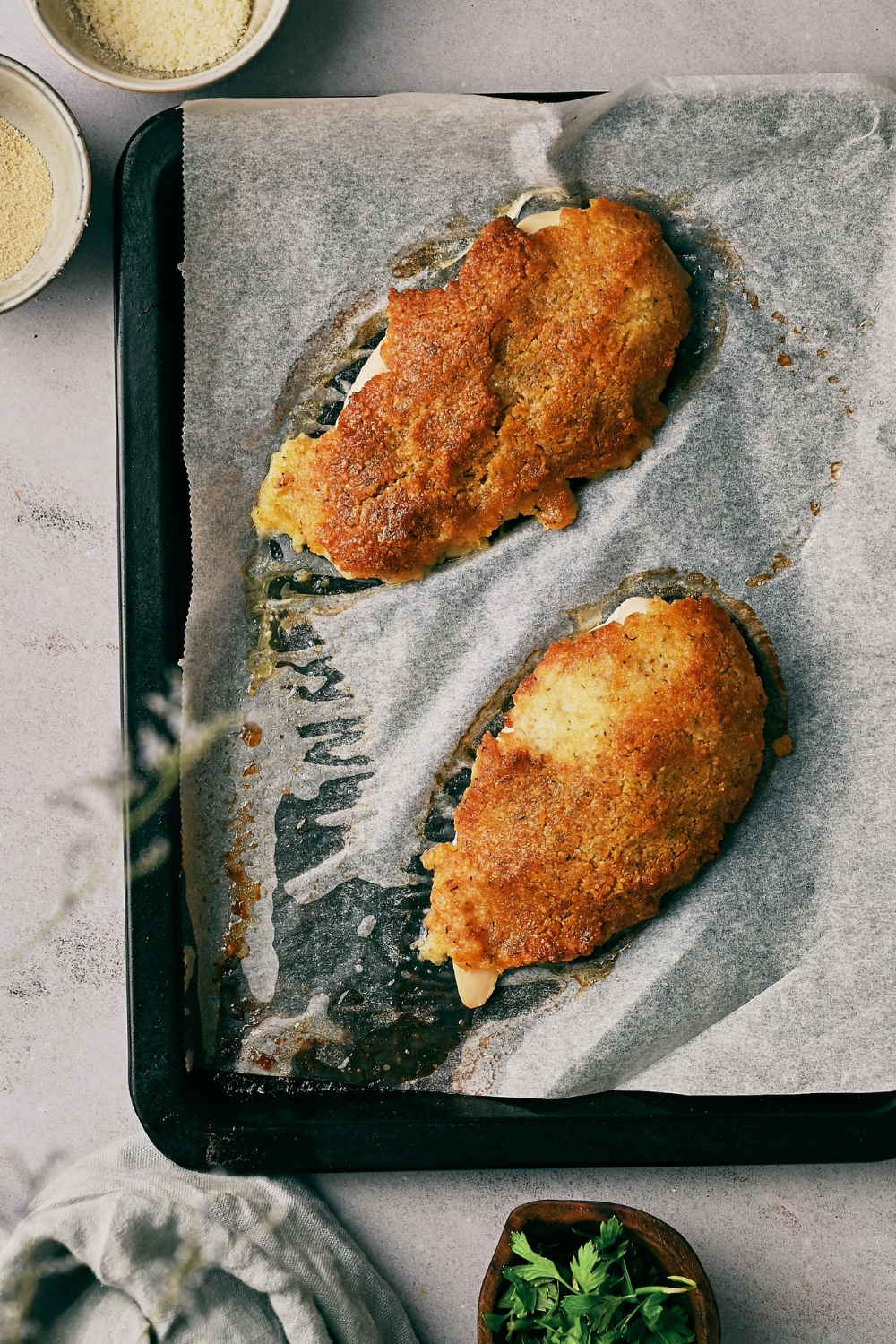 Two freshly baked and breaded chicken breasts on a baking sheet lined with parchment paper.