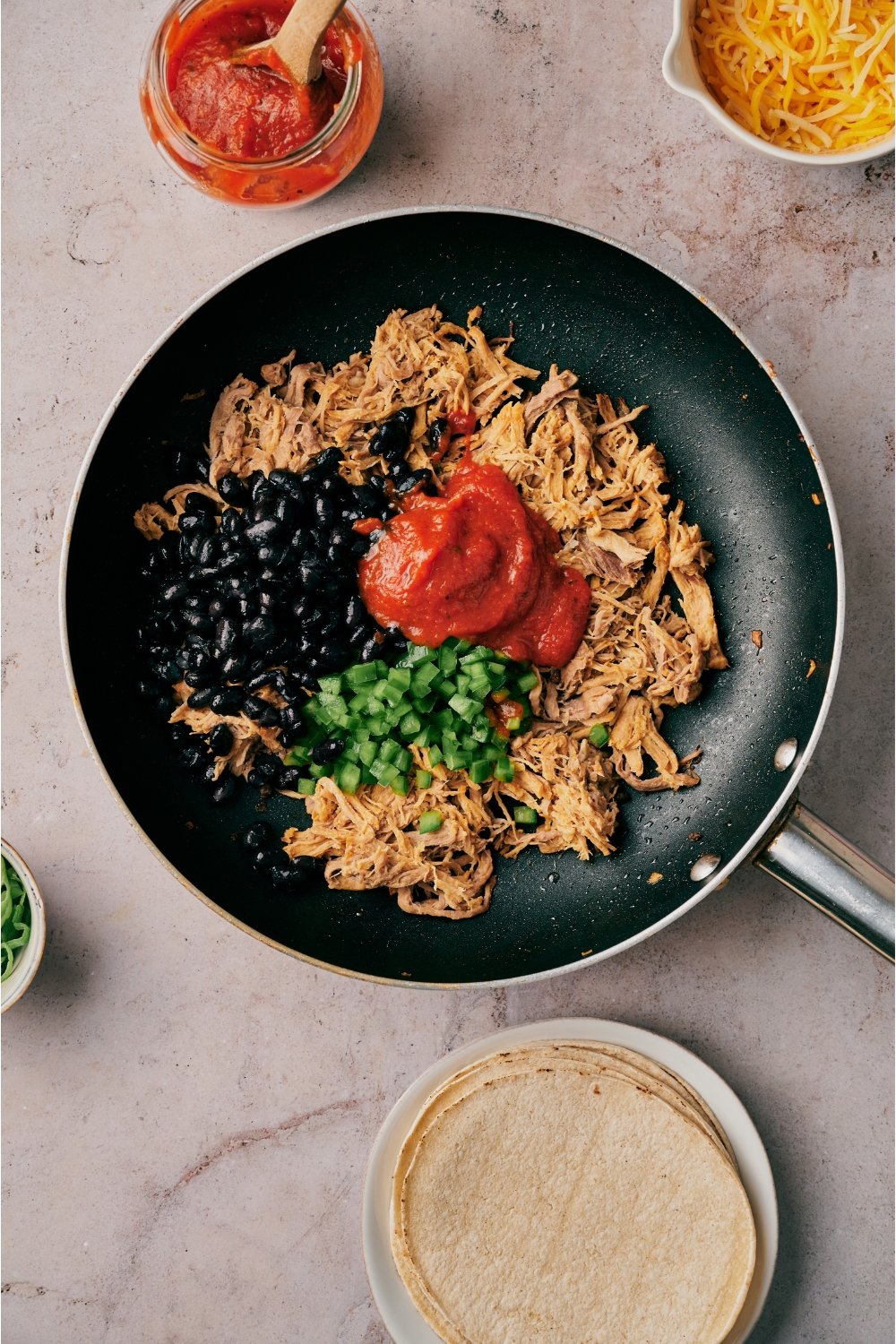 A skillet filled with cooked shredded pork, black beans, tomato sauce, and diced bell pepper.