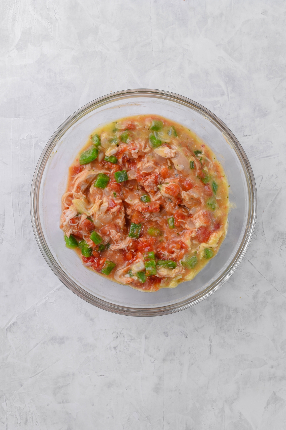 A clear bowl filled with diced peppers, onions, shredded chicken, and diced tomatoes in a creamy sauce.