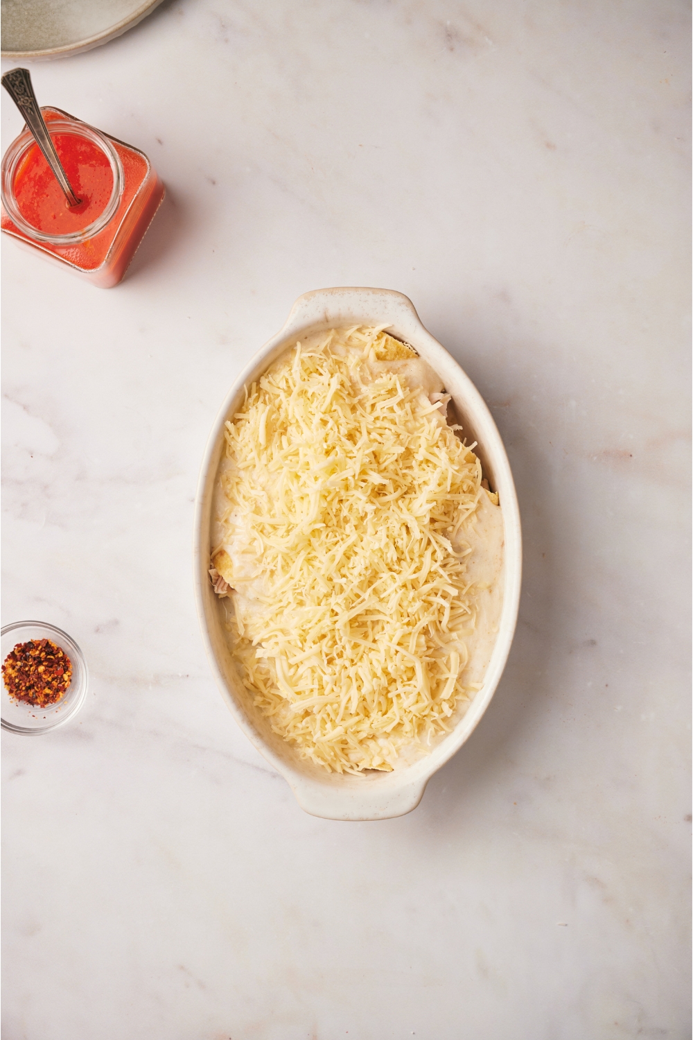 A baking dish filled with unbaked chicken enchiladas covered in shredded cheese.