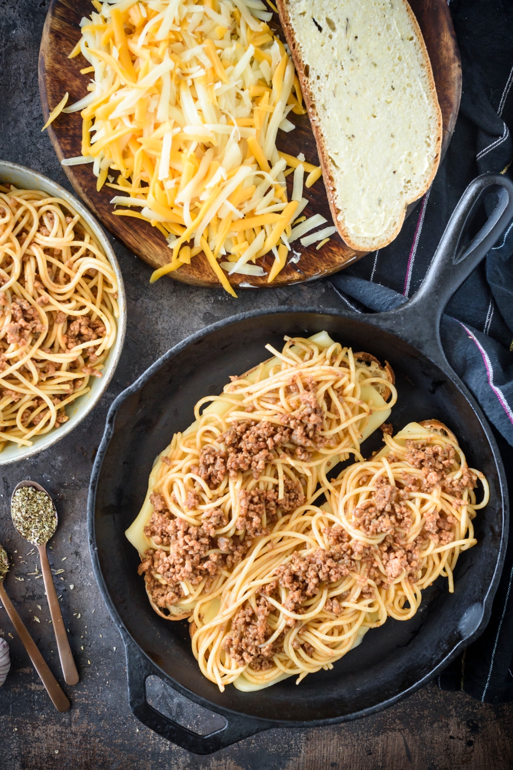 Two pieces of toast topped with cheese and spaghetti in meat sauce in a cast iron skillet.