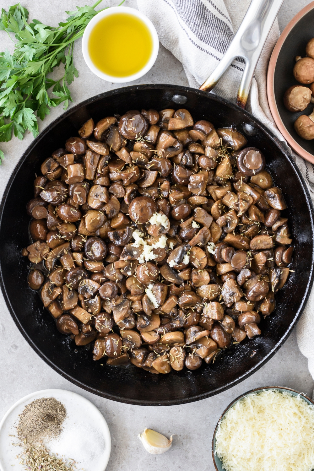 A skillet filled with cooked mushroom slices and minced garlic added but not yet mixed together.