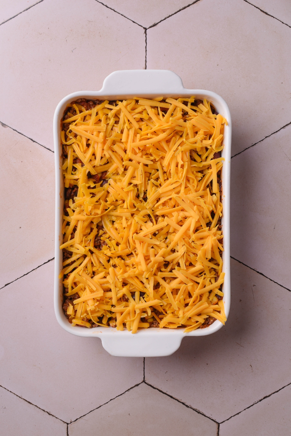 A baking dish filled with unbaked taco casserole covered in shredded cheese.