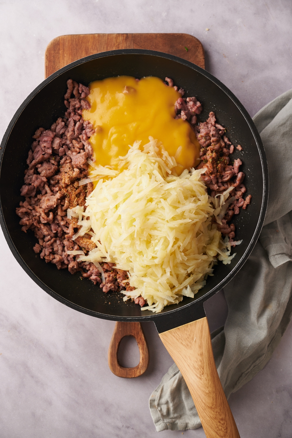 A skillet filled with cooked ground beef, seasoning, hash browns, and condensed soup.