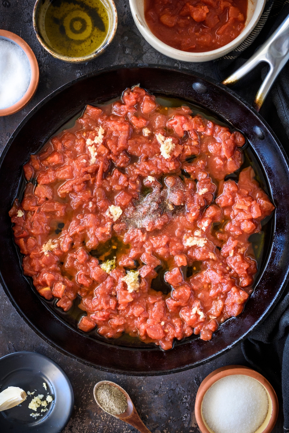 A skillet with canned tomatoes in juices cooking with garlic and seasonings.