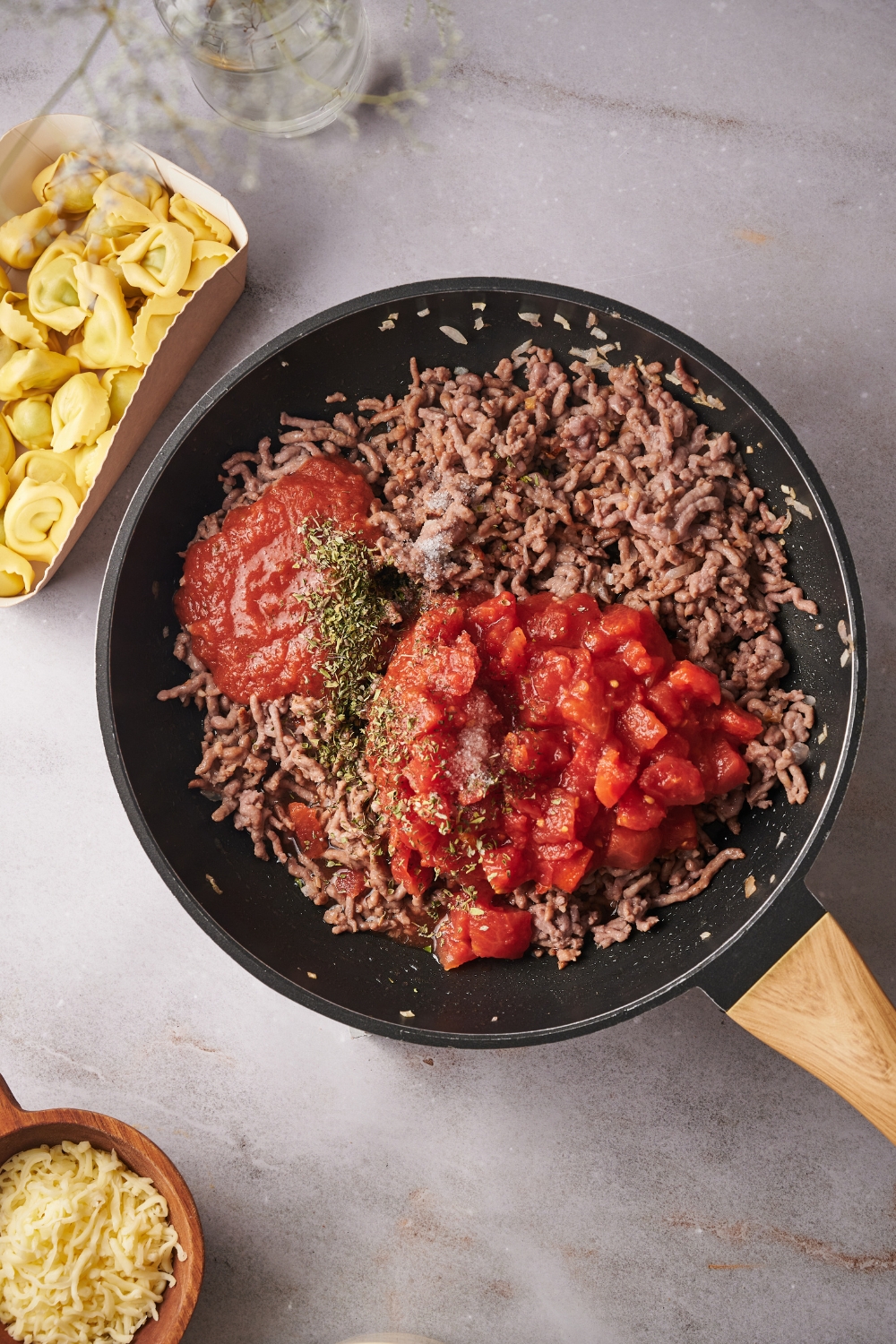 A skillet filled with cooked ground beef, seasonings, tomato sauce, and crushed tomatoes.