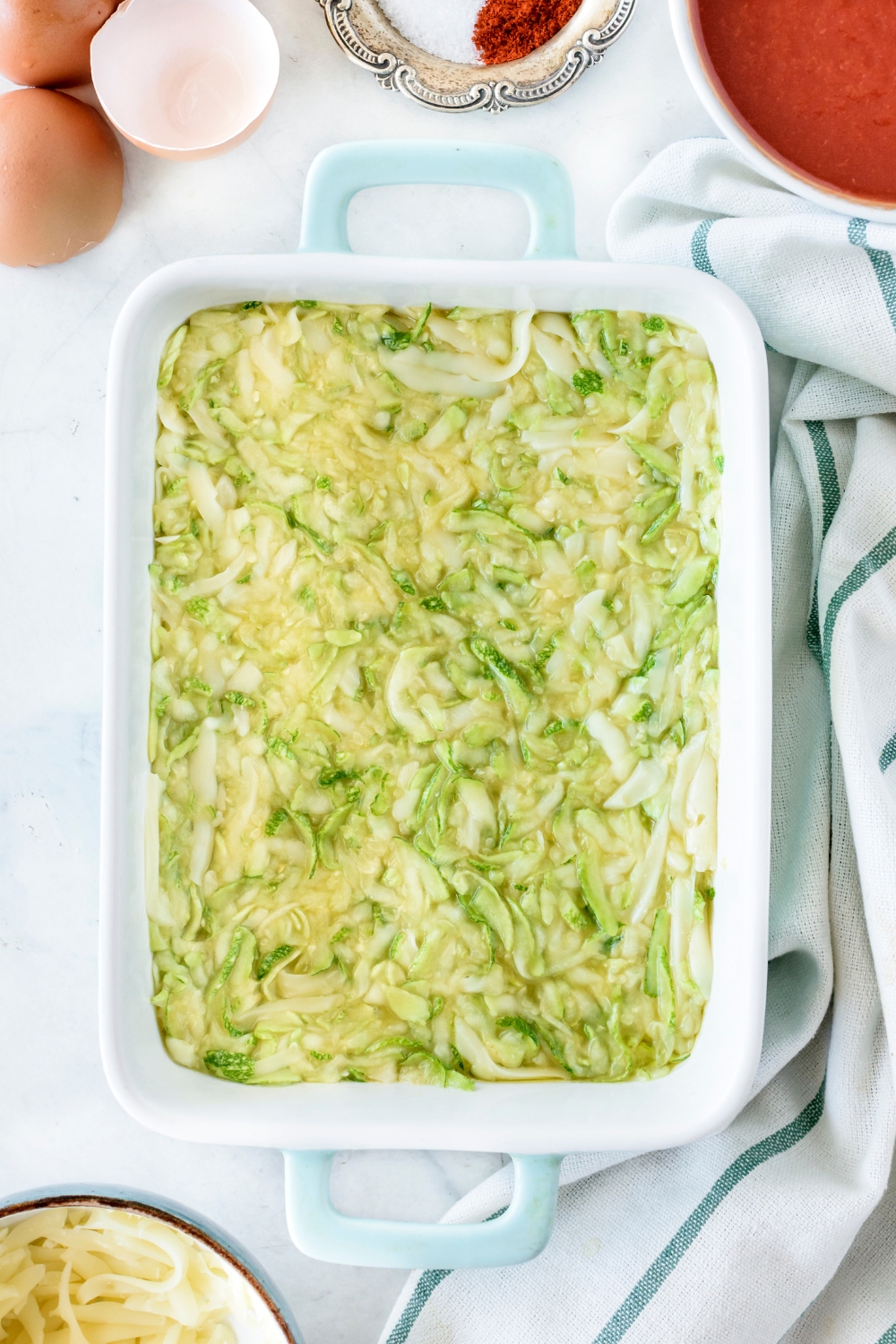 A baking dish filled with grated zucchini spread into an even layer.
