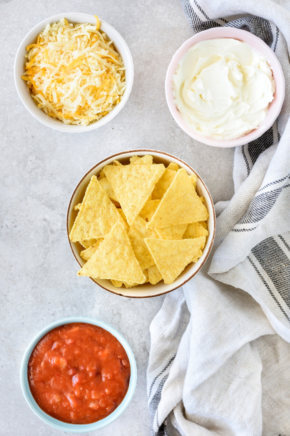 An assortment of ingredients including bowls of tortilla chips, cream cheese, shredded cheese, and chili.
