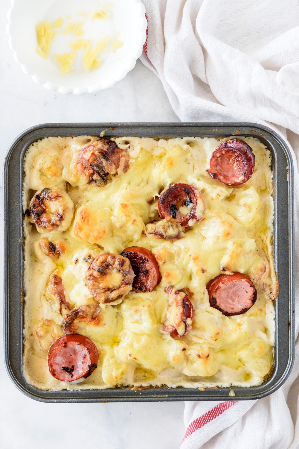 A baking dish filled with freshly baked sausage casserole. The casserole is golden brown and the sausages are browned and crispy.