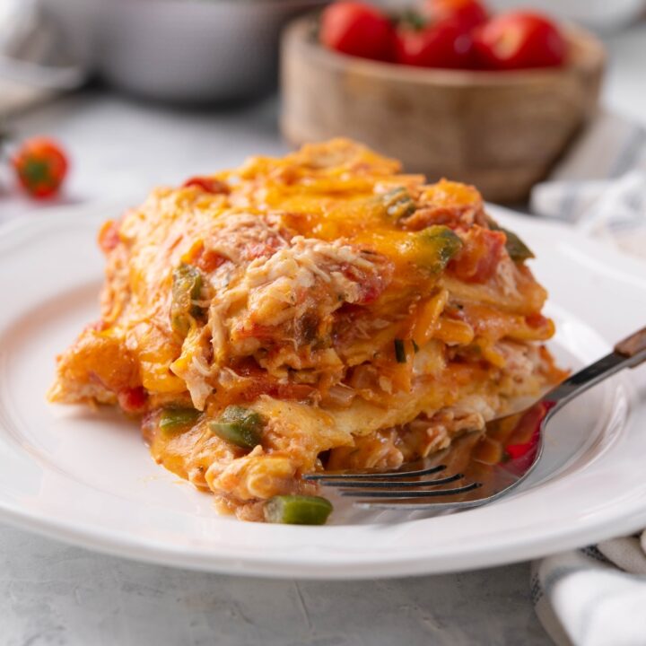 A square serving of king ranch chicken casserole covered in melted cheese with a fork on the plate.