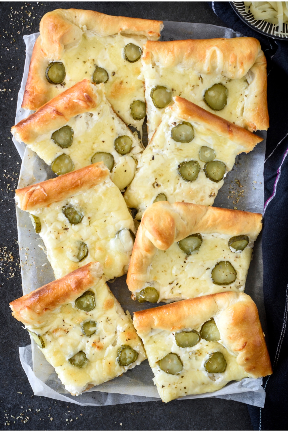 Pickle pizza cut into eight equal-sized squares layered on top of each other on a sheet of parchment paper.