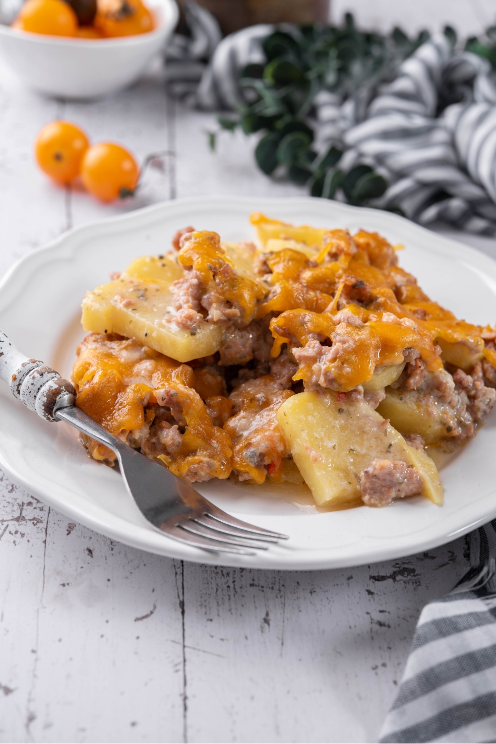 A serving of sausage and potato casserole covered in melted cheese on a plate with a fork next to it.