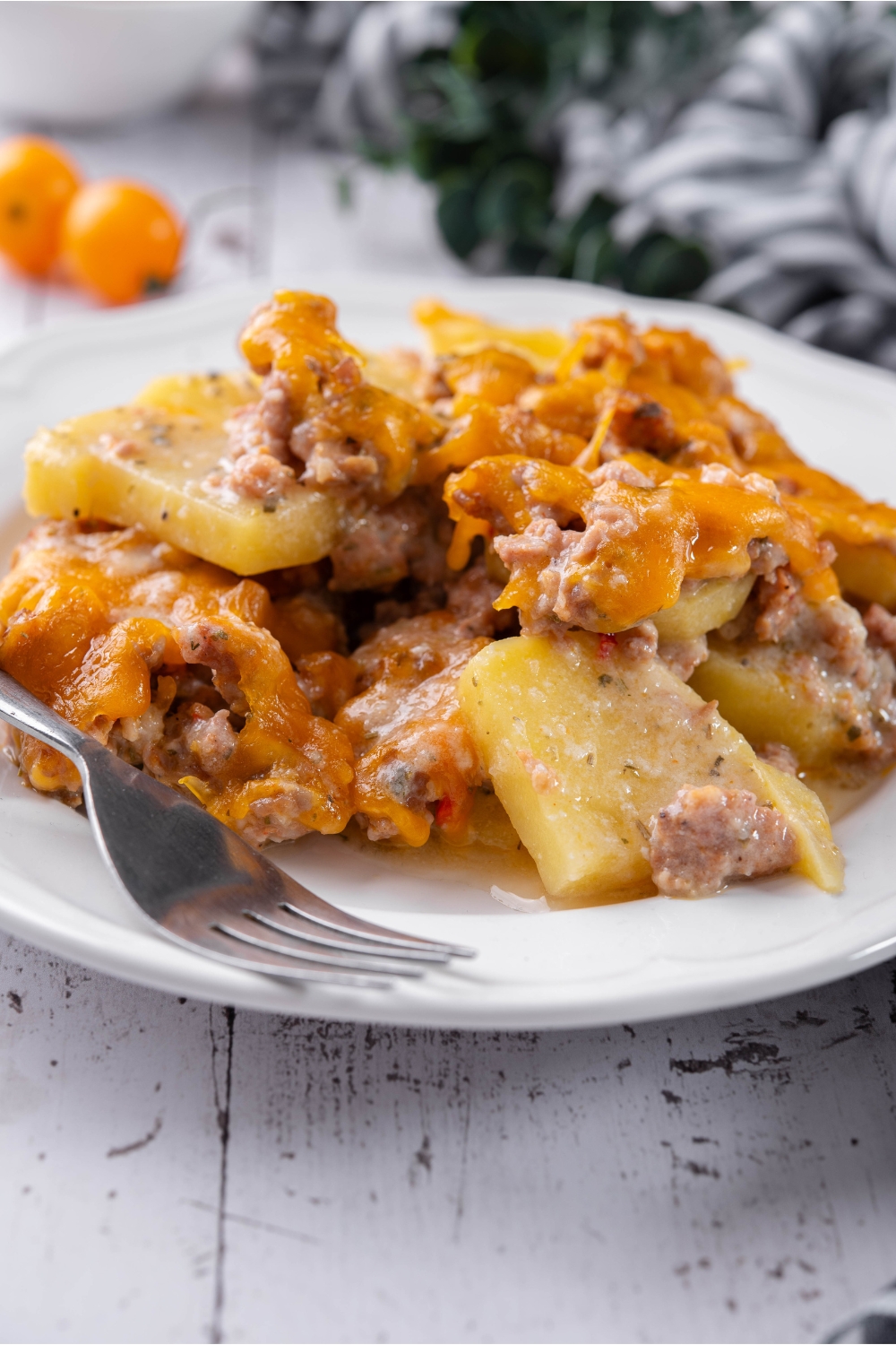 A serving of sausage and potato casserole covered in melted cheese on a plate with a fork next to it.