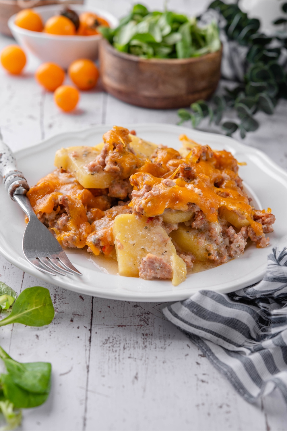 A serving of sausage and potato casserole covered in melted cheese on a plate with a fork next to it.