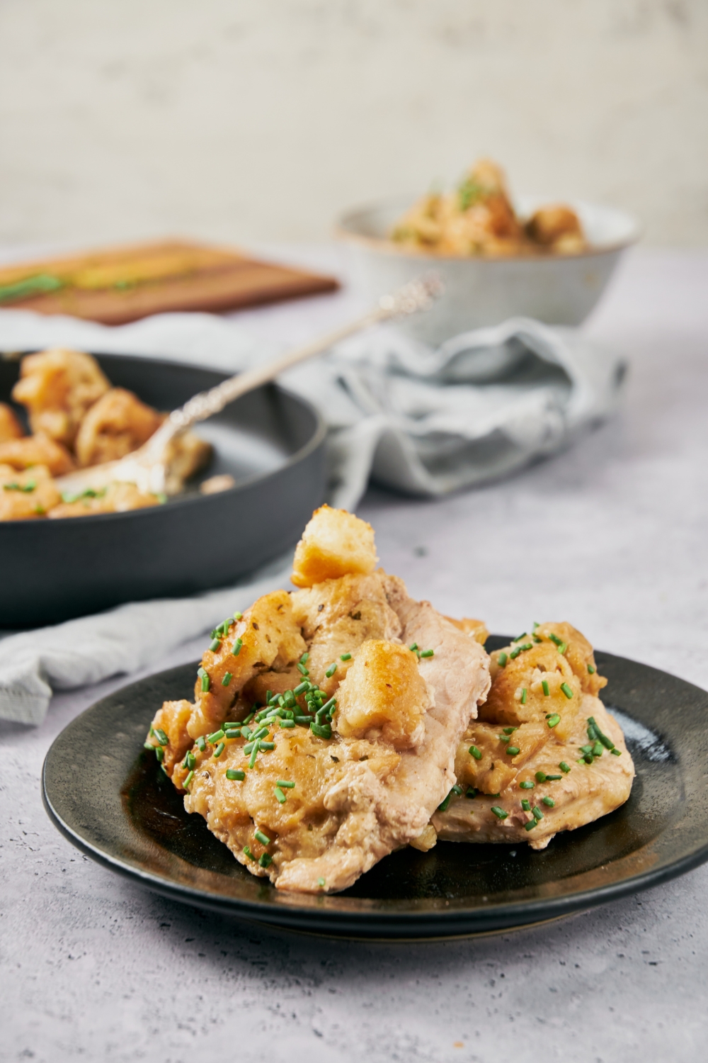 Two pork chops stacked on each other and each is covered in a creamy sauce with stuffing and a garnish of chopped chives.