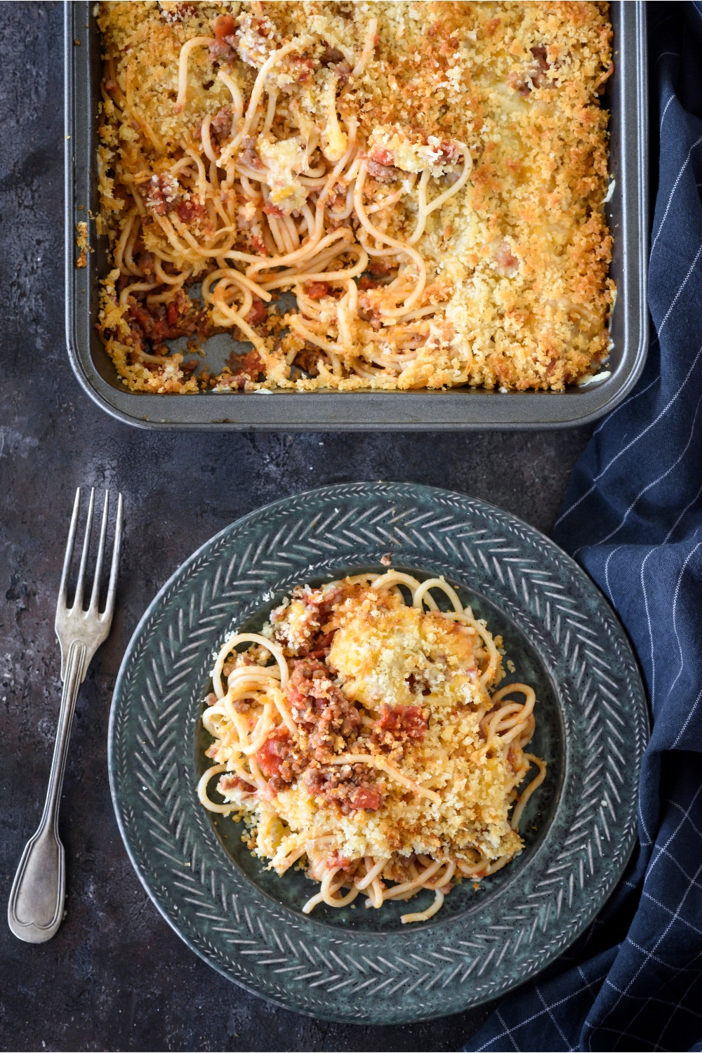 A serving of spaghetti casserole piled high next to a fork and the rest of the casserole.