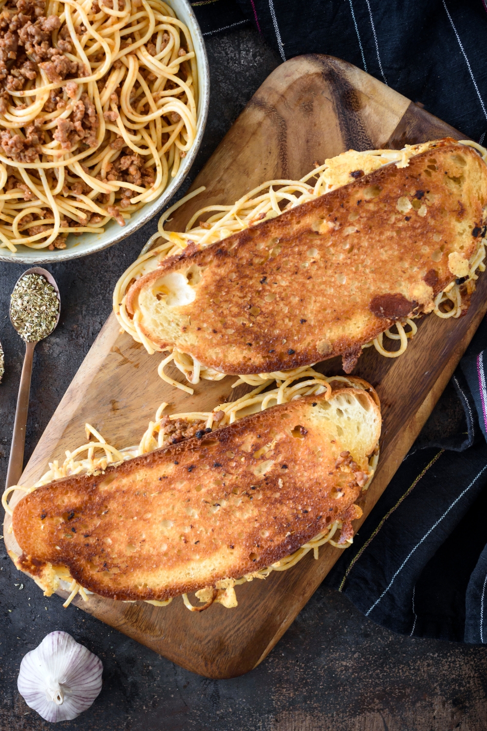 Two spaghetti sandwiches on a cutting board with spaghetti noodles spilling out the sides.