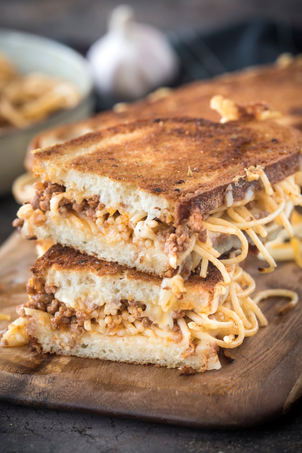 A spaghetti sandwich cut in half and each half is stacked on top of each other. Spaghetti noodles are spilling out of the sides of the bread.