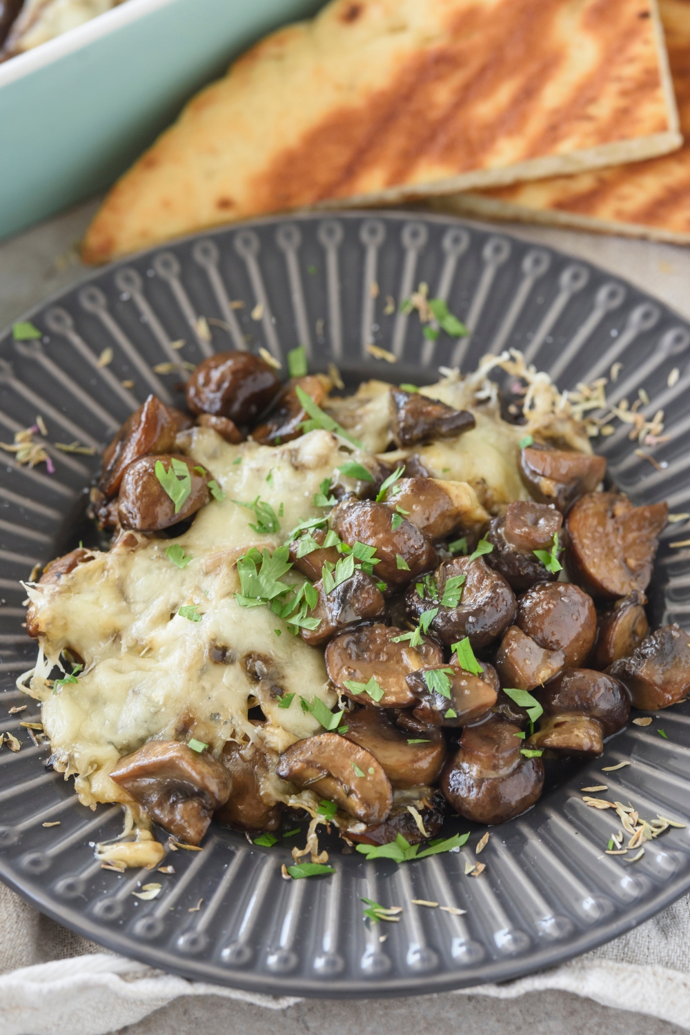 A plate of mushroom casserole covered in melted cheese and fresh herbs.