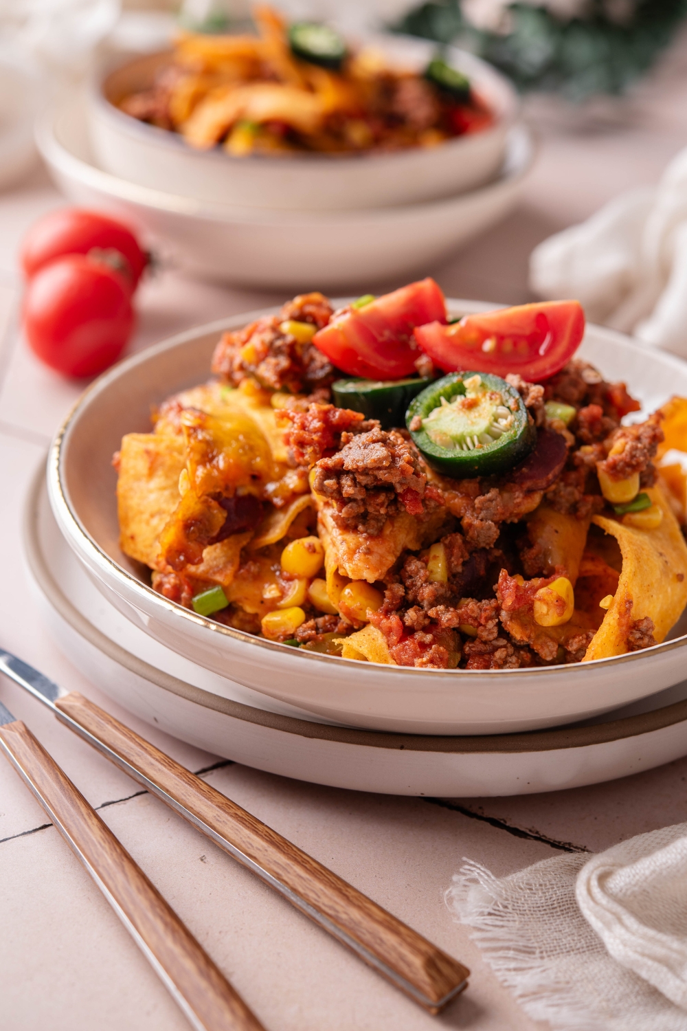A bowl of Frito taco casserole topped with melted cheese, diced tomatoes, and sliced jalapeños.
