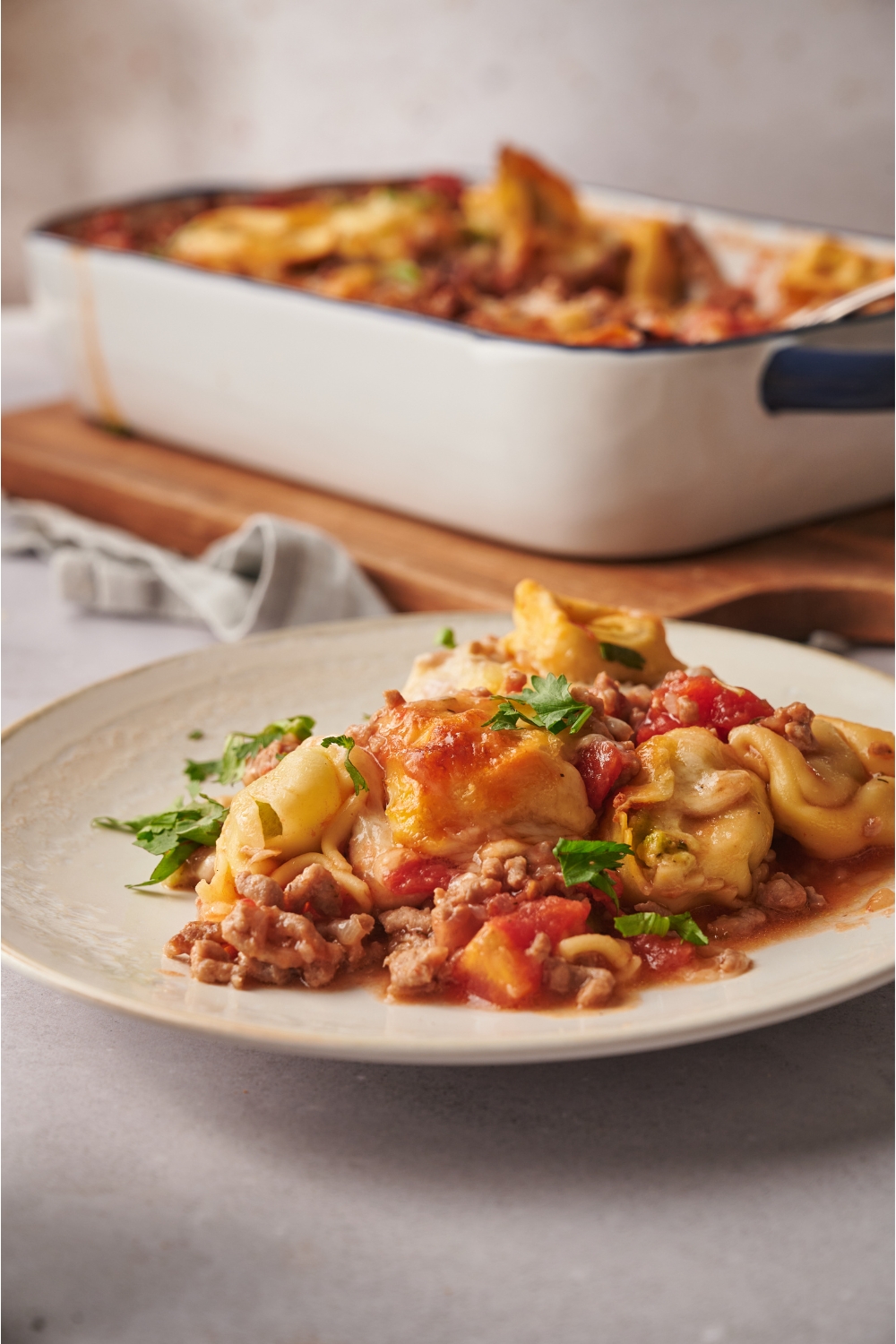 A serving of tortellini casserole with chunks of ground beef, cooked tomatoes, melted cheese, and fresh herbs.