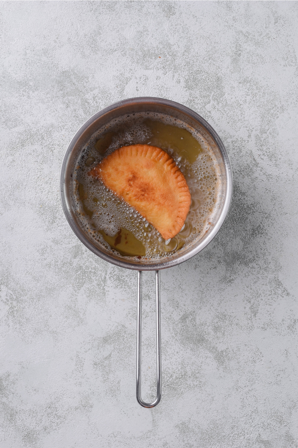 A pot with an apple pie being fried in oil.