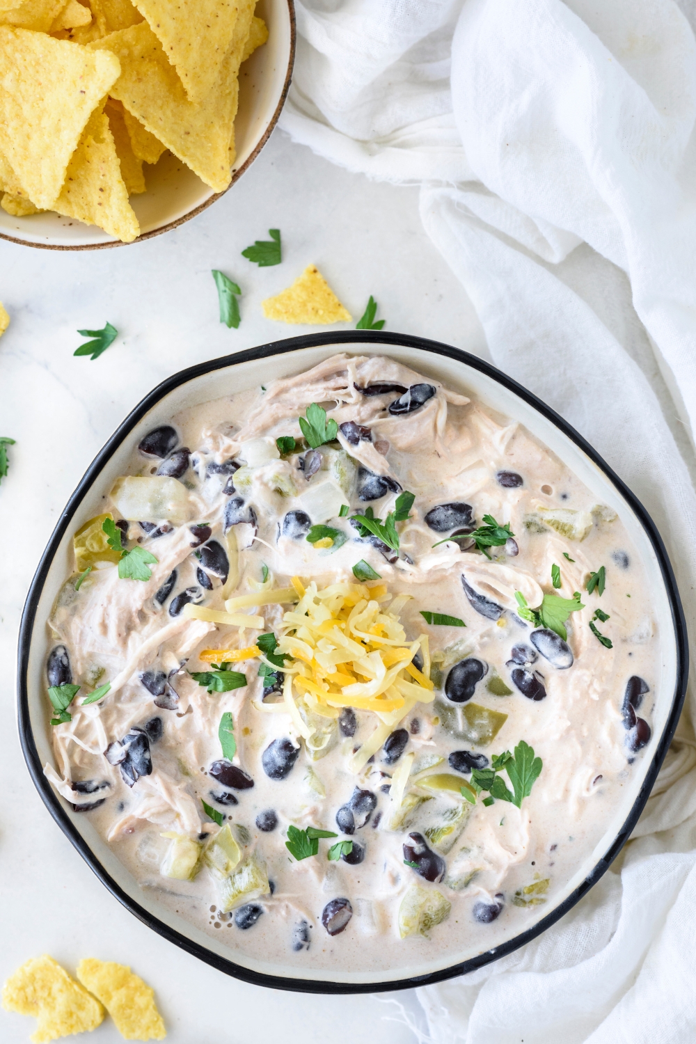 A bowl of white chicken chili with parsley and black beans in the chili and shredded cheese is garnished on top.